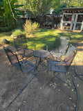 Four black metal mesh spring chairs arranged around a round mesh-top patio table.