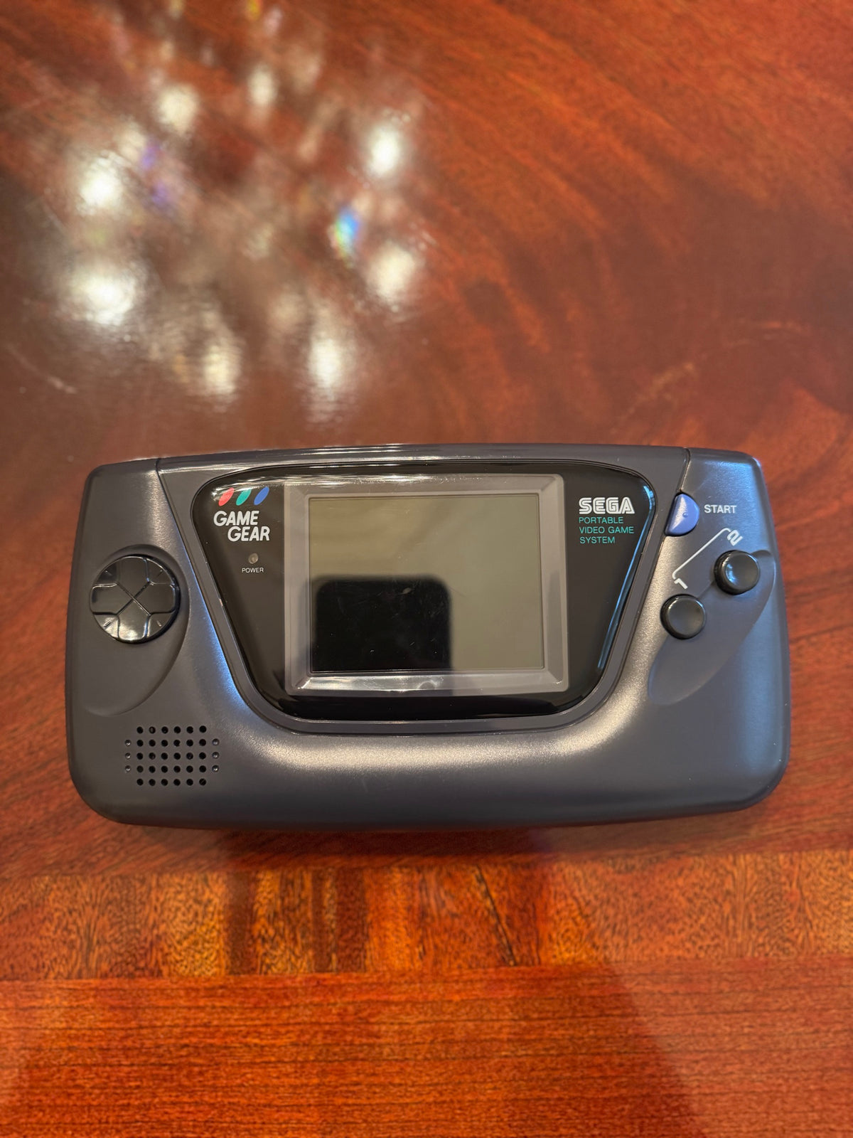 Front of a black Sega Game Gear handheld with screen, directional pad, and Start button