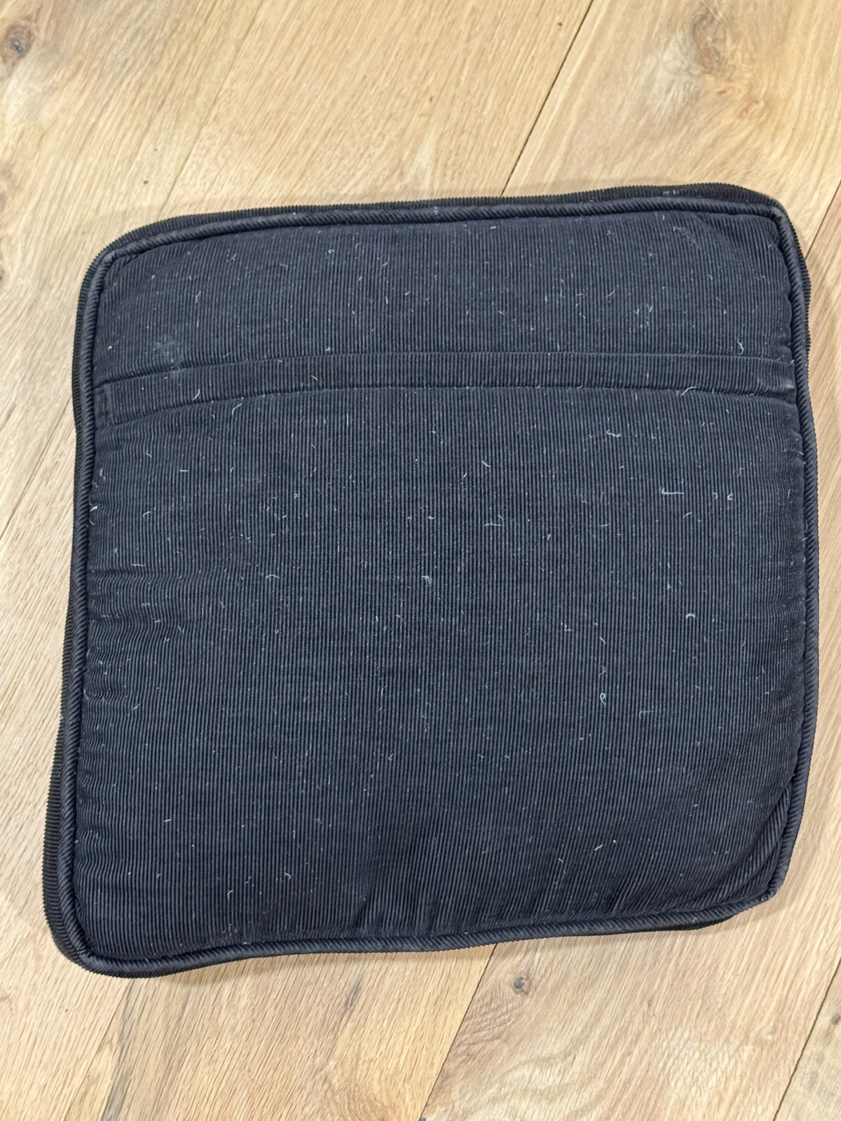 Dark navy blue corduroy pillow back with visible seams and zipper, laid flat on light wood flooring