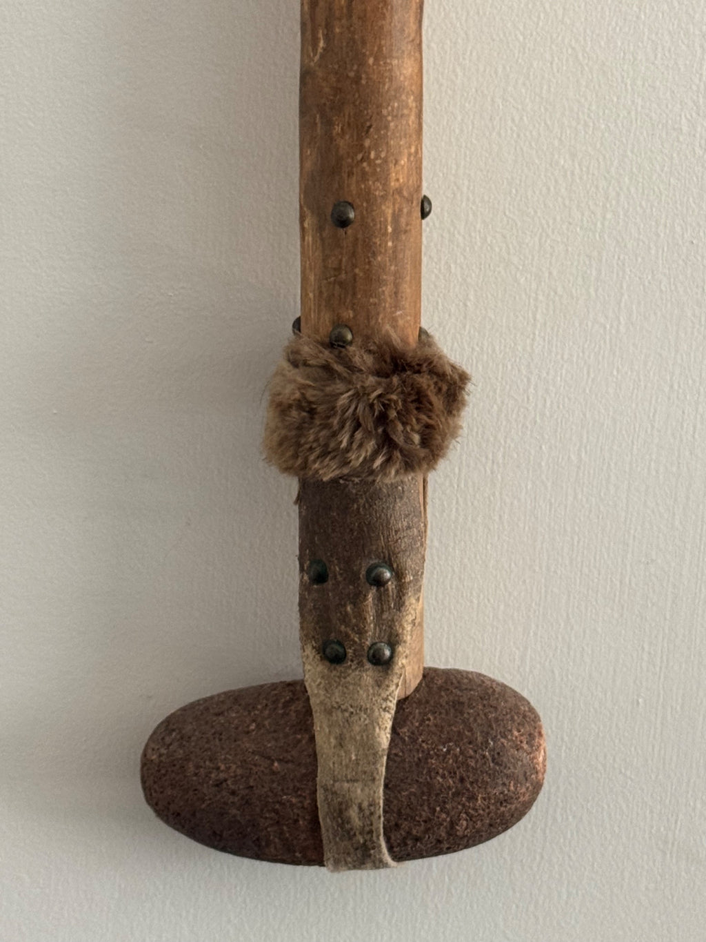 Close-up detail of middle section showing wooden shaft with small metal studs, fur binding wrapped around shaft, and iron base attachment