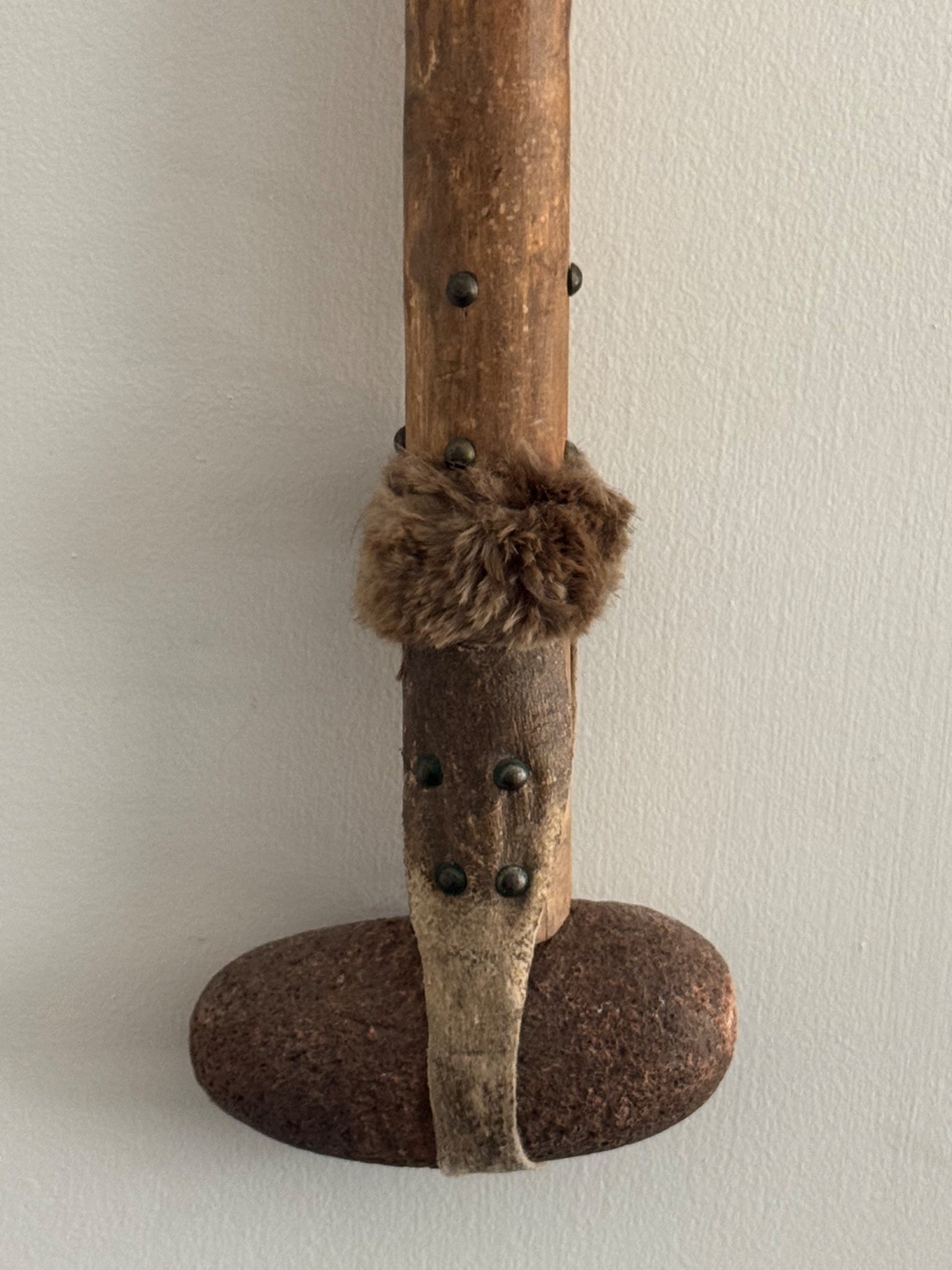 Close-up detail of middle section showing wooden shaft with small metal studs, fur binding wrapped around shaft, and iron base attachment