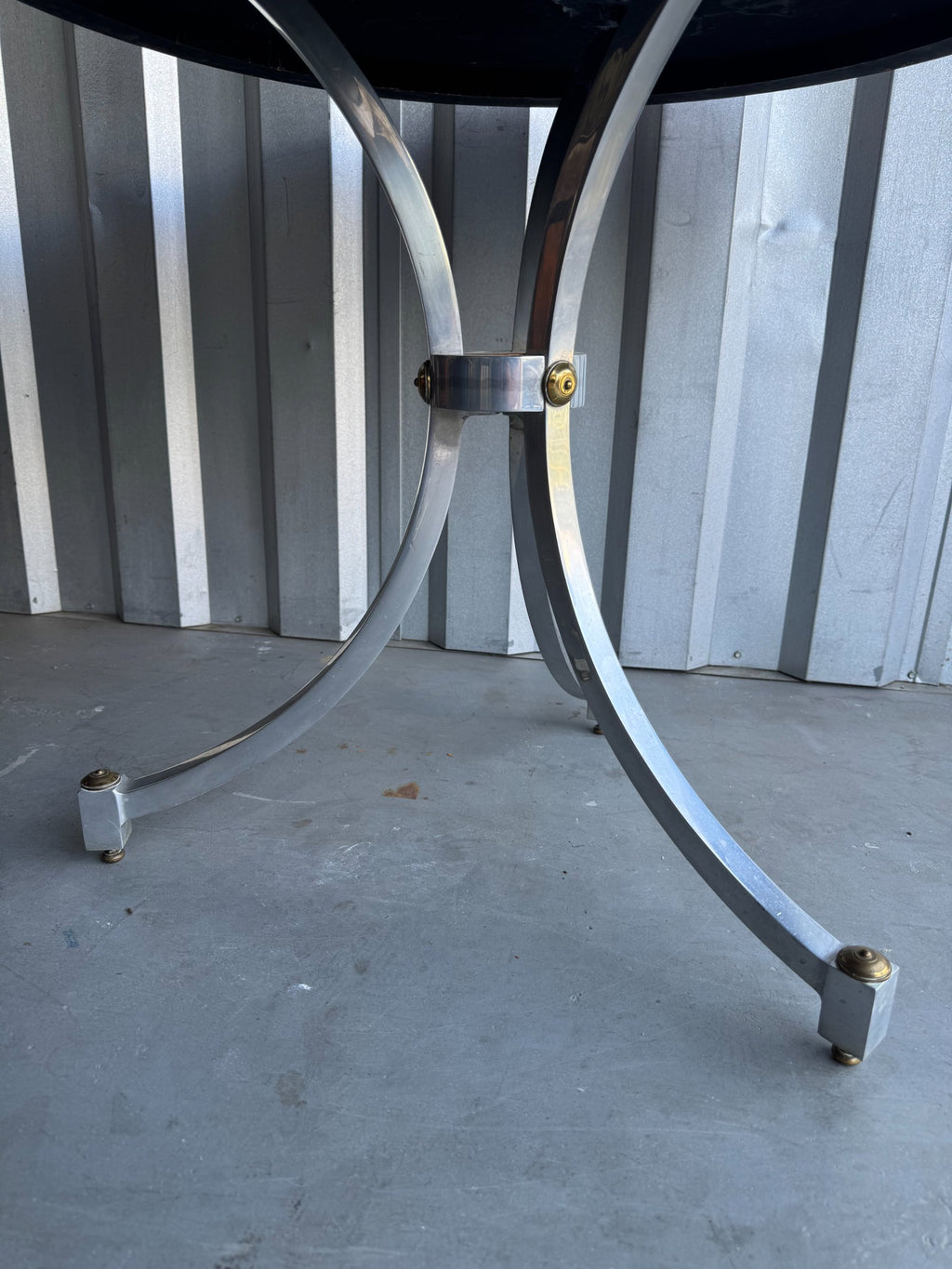 Full table base assembly showing two curved chrome legs meeting at center band with brass hardware