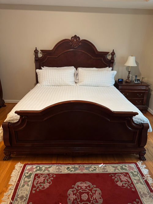 Carved mahogany-finish king bed with arched headboard, pineapple finials, and matching footboard in a bedroom setting