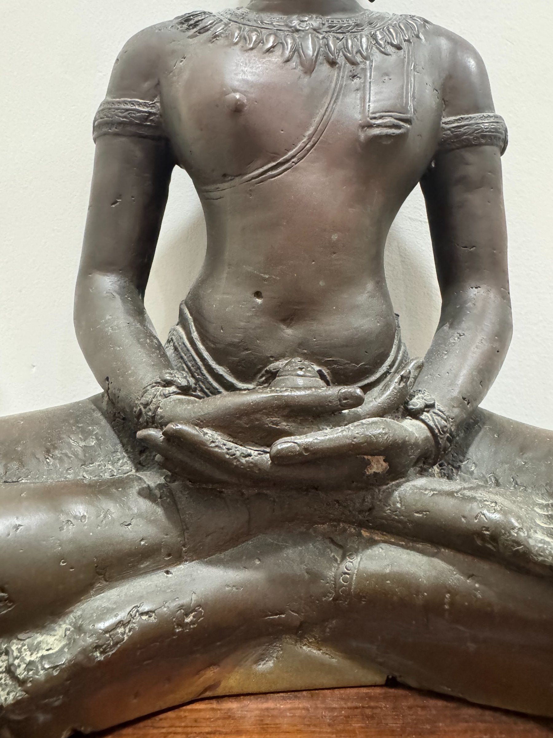 Close-up detail of Buddha torso showing draped robe, decorative chest ornaments, and arm positioning