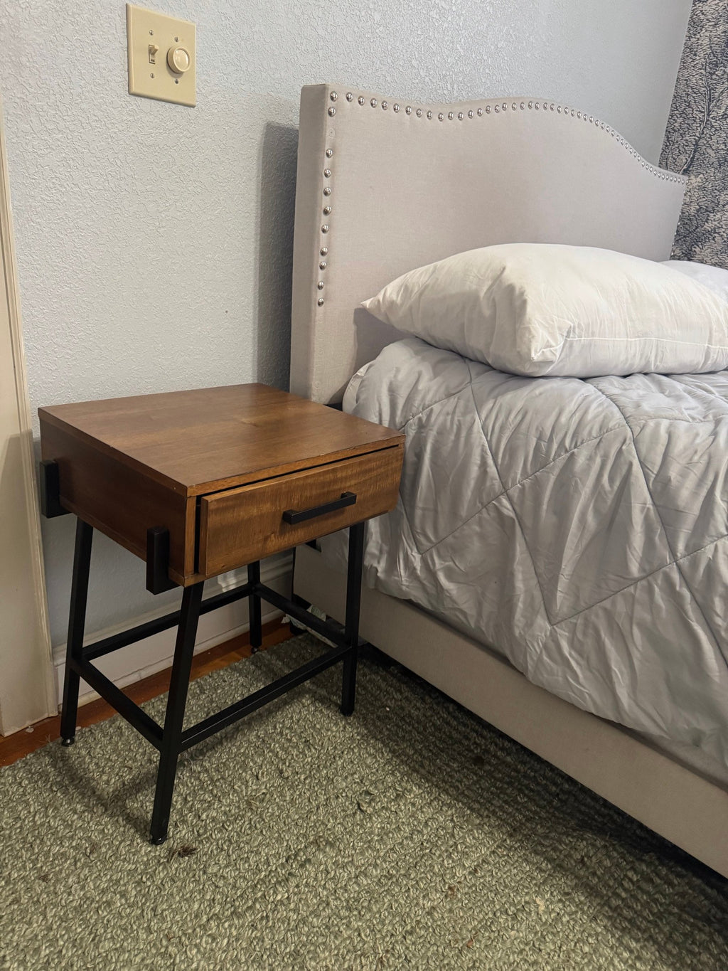 Wood one-drawer nightstand on a black metal base next to a bed