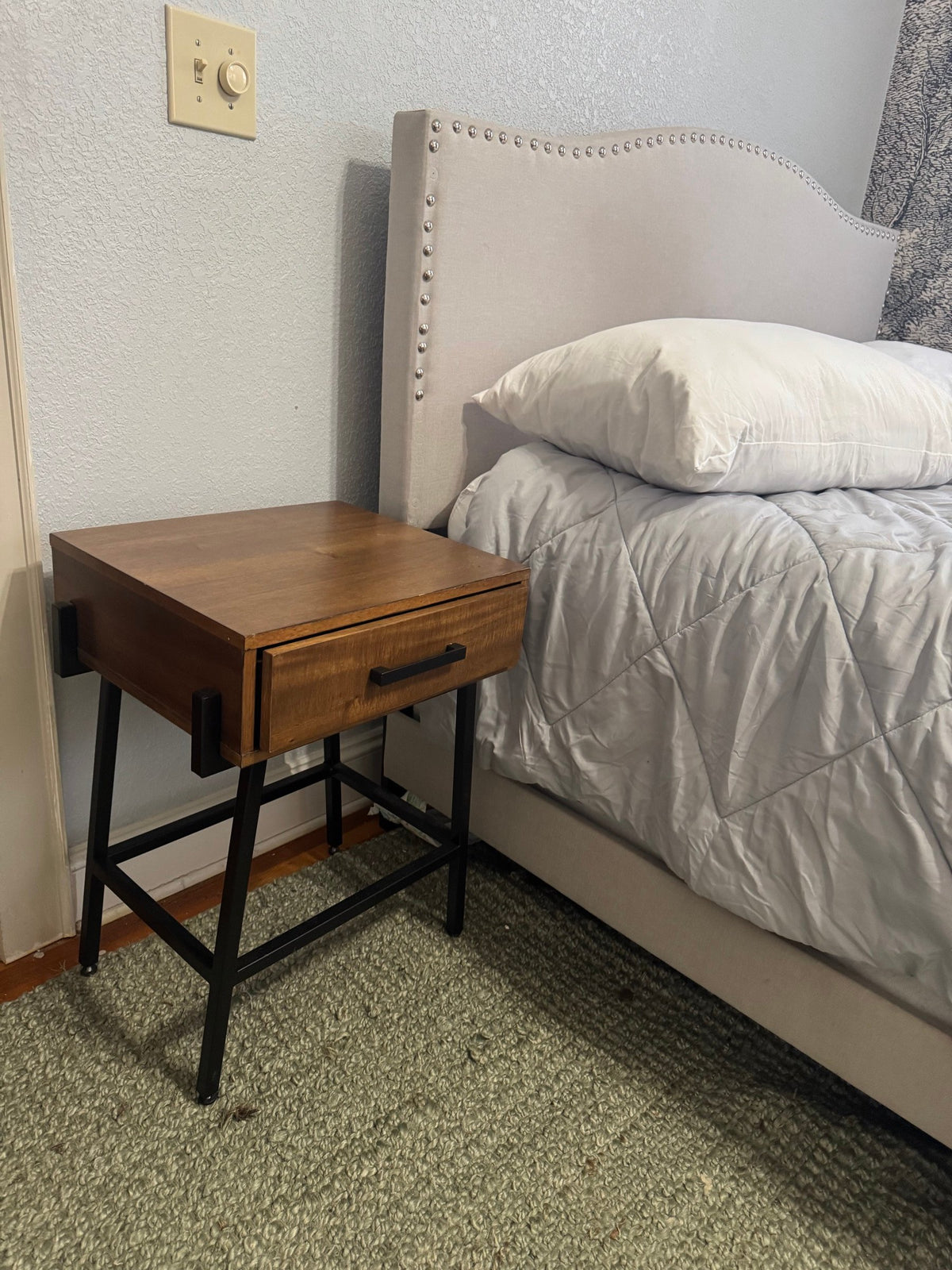 Wood one-drawer nightstand on a black metal base next to a bed