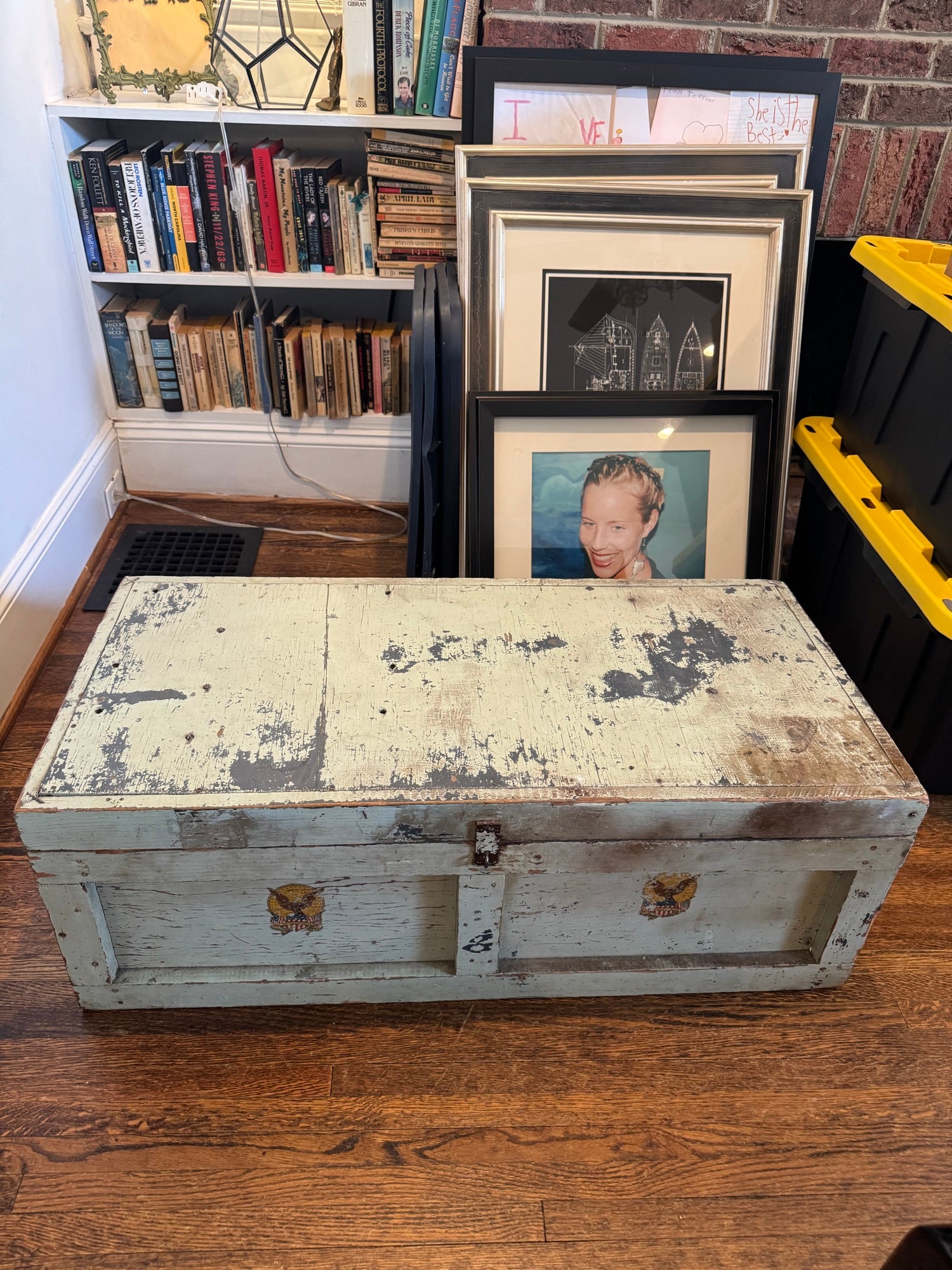 Trunk displayed closed in home setting on wooden floor, showing full front view with cream painted exterior and metal clasps