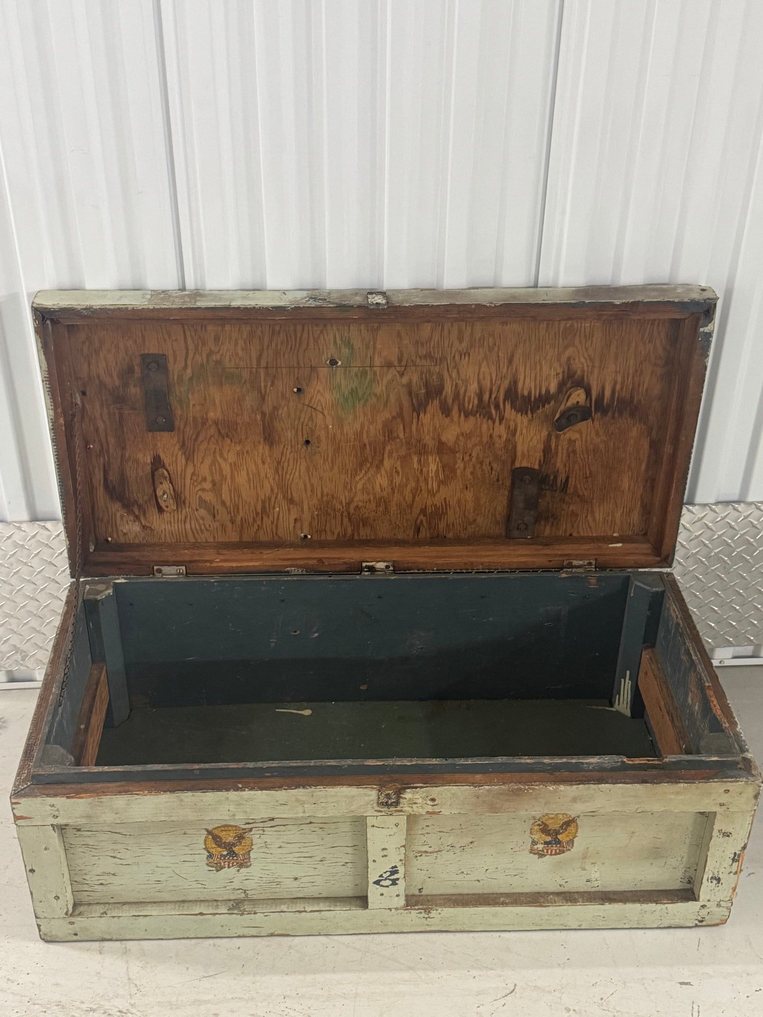 Interior view of open trunk showing dark wood-paneled lid and green canvas-lined base with metal reinforcements