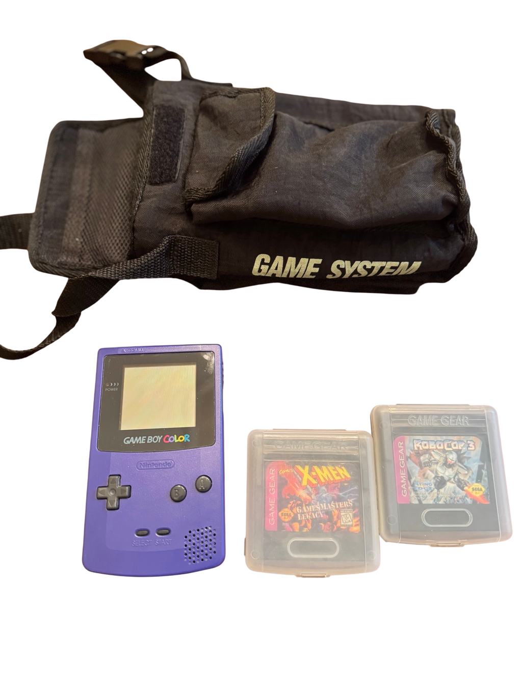Purple Nintendo Game Boy Color, two Sega Game Gear cartridges, and a black carrying pouch labeled Game System on a wood table