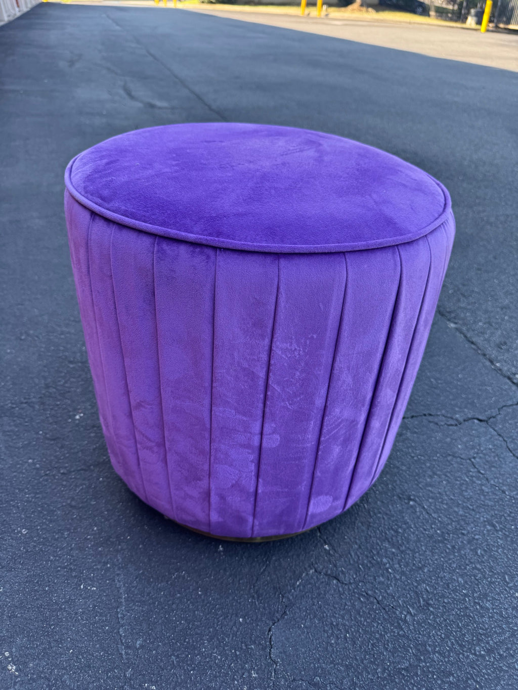 Purple velvet channel-tufted round ottoman pouf on dark floor, front view showing complete piece