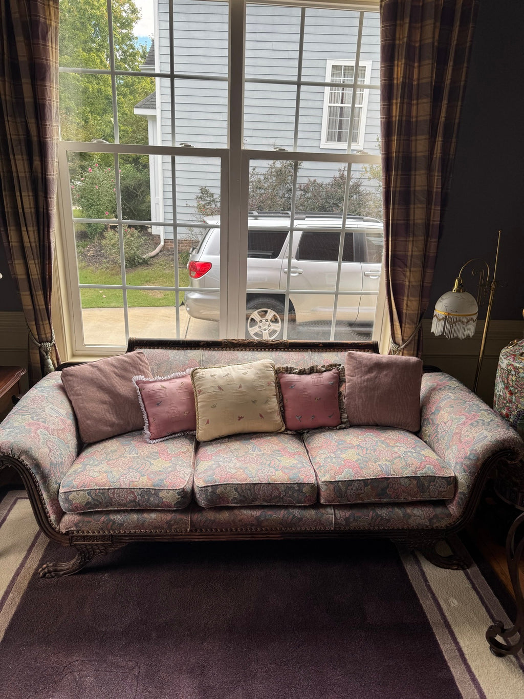 Full front view of the carved sofa in situ beneath a window, with decorative pillows