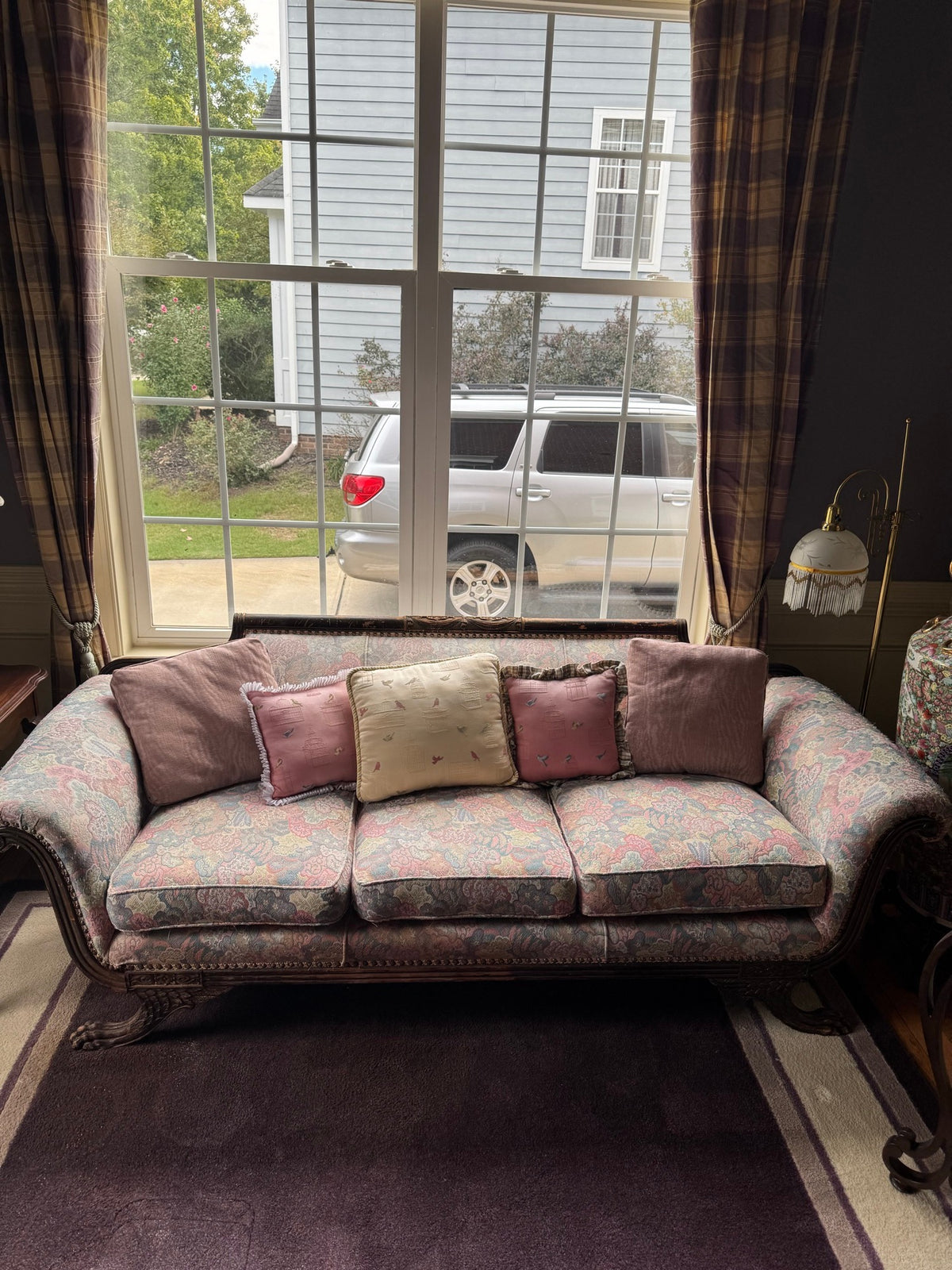 Full front view of the carved sofa in situ beneath a window, with decorative pillows
