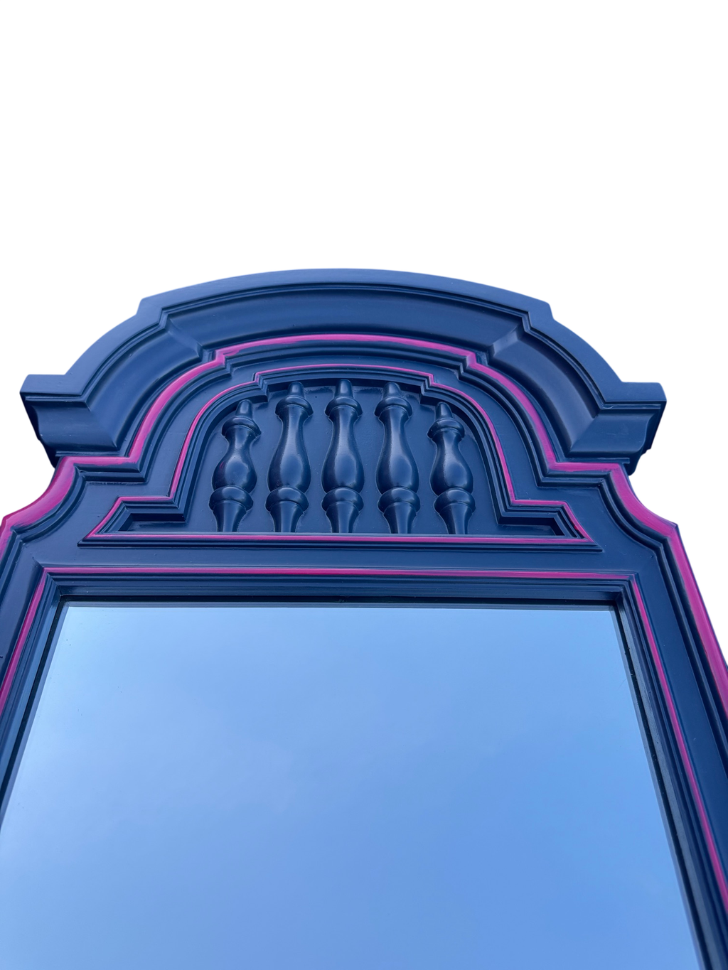 Navy blue arched mirror with pink trim and decorative spindle detail at top, against clear sky