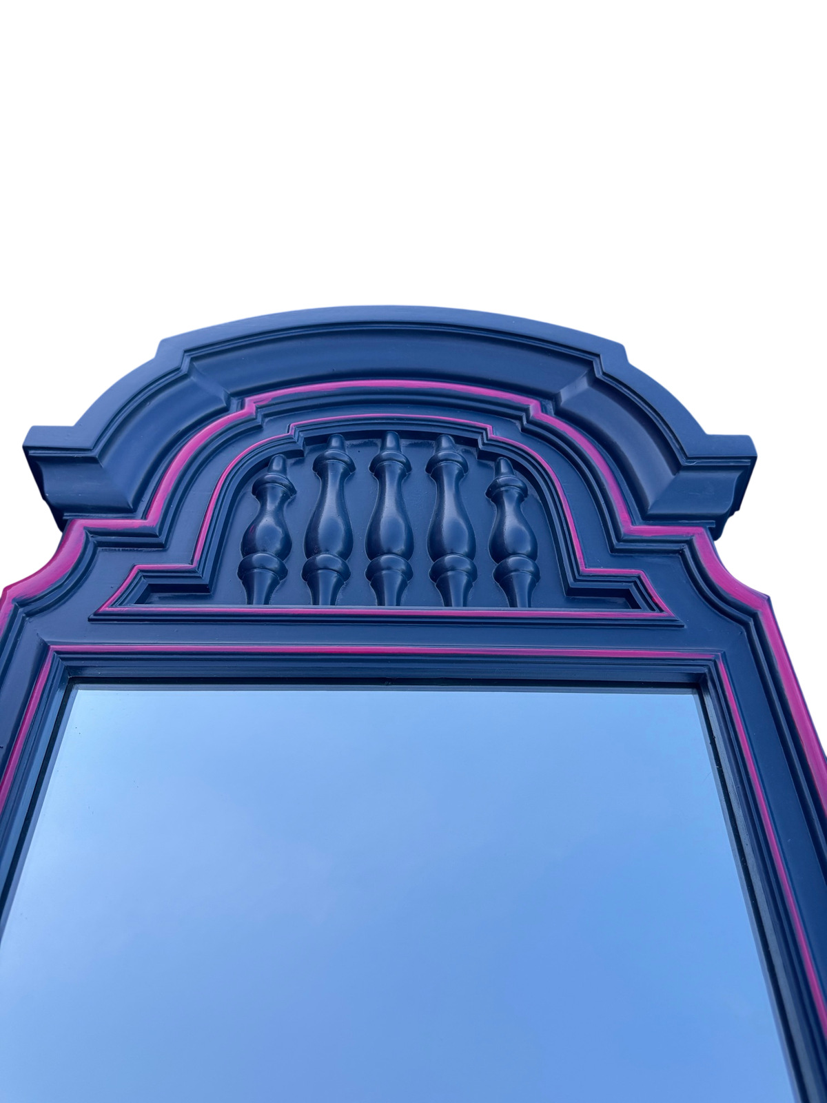 Navy blue arched mirror with pink trim and decorative spindle detail at top, against clear sky
