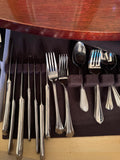 Row of stainless knives, forks and spoons in a felt-lined flatware chest under a wood table