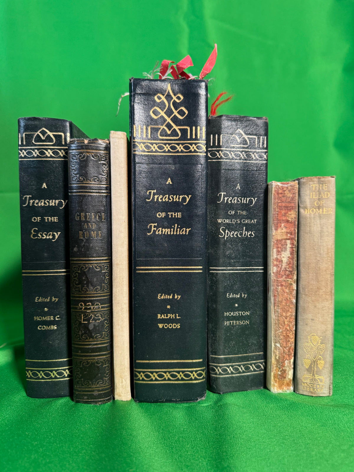 Three matching gilt-stamped Treasury anthologies — the Essay, the Familiar and the World's Great Speeches — stood on green cloth with Greece and Rome and a Modern Library Iliad of Homer