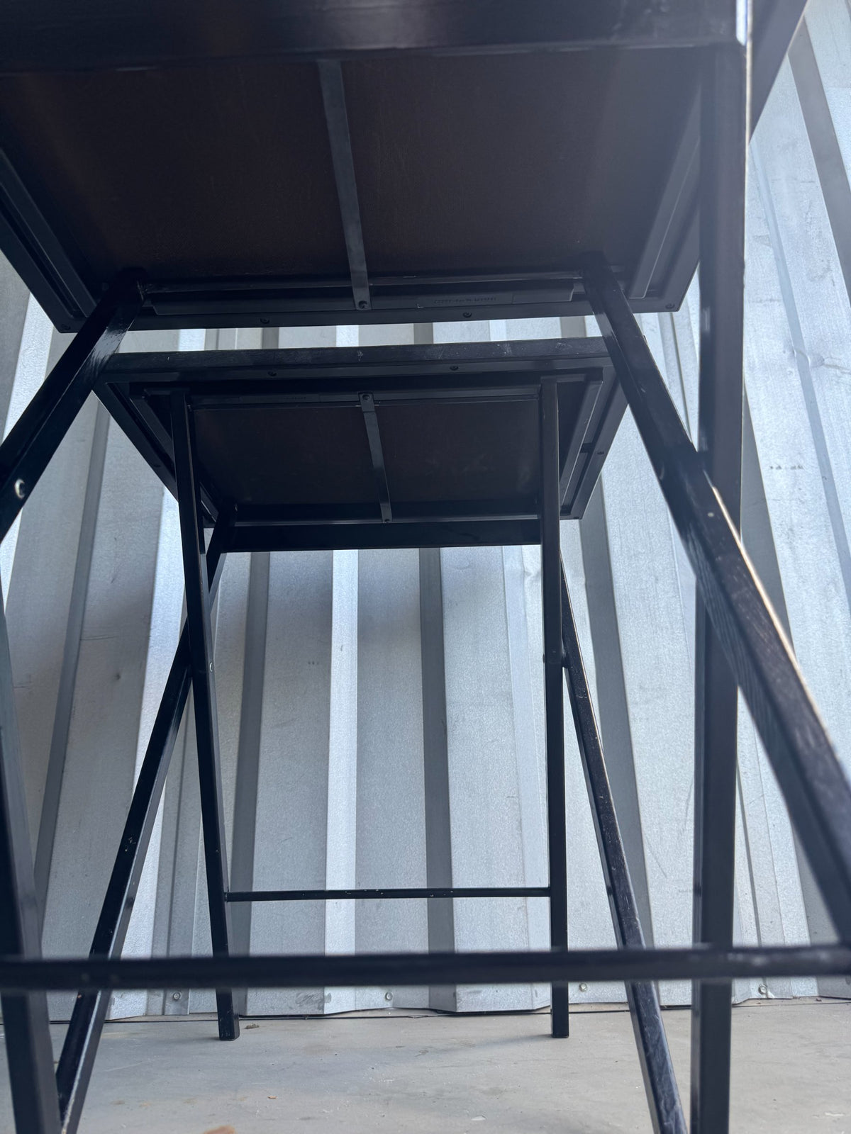 Interior view looking up at stacked nesting tables, showing black metal frame and legs supporting transparent glass-topped surfaces