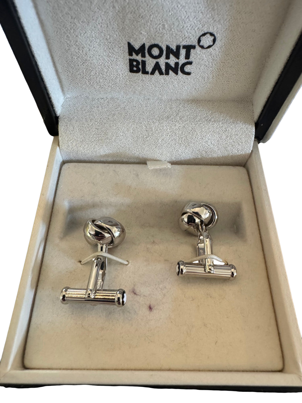Montblanc branded presentation box open, displaying pair of silver-toned knot cufflinks on cream velvet interior