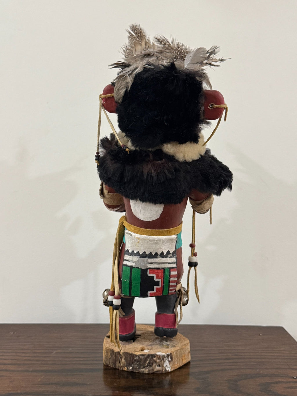 Back view displaying black fur back piece, feathered headdress, and lower body costume with geometric painted patterns
