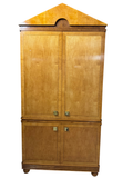 Full front view of blonde wood two-door armoire with pediment top and decorative inlay trim