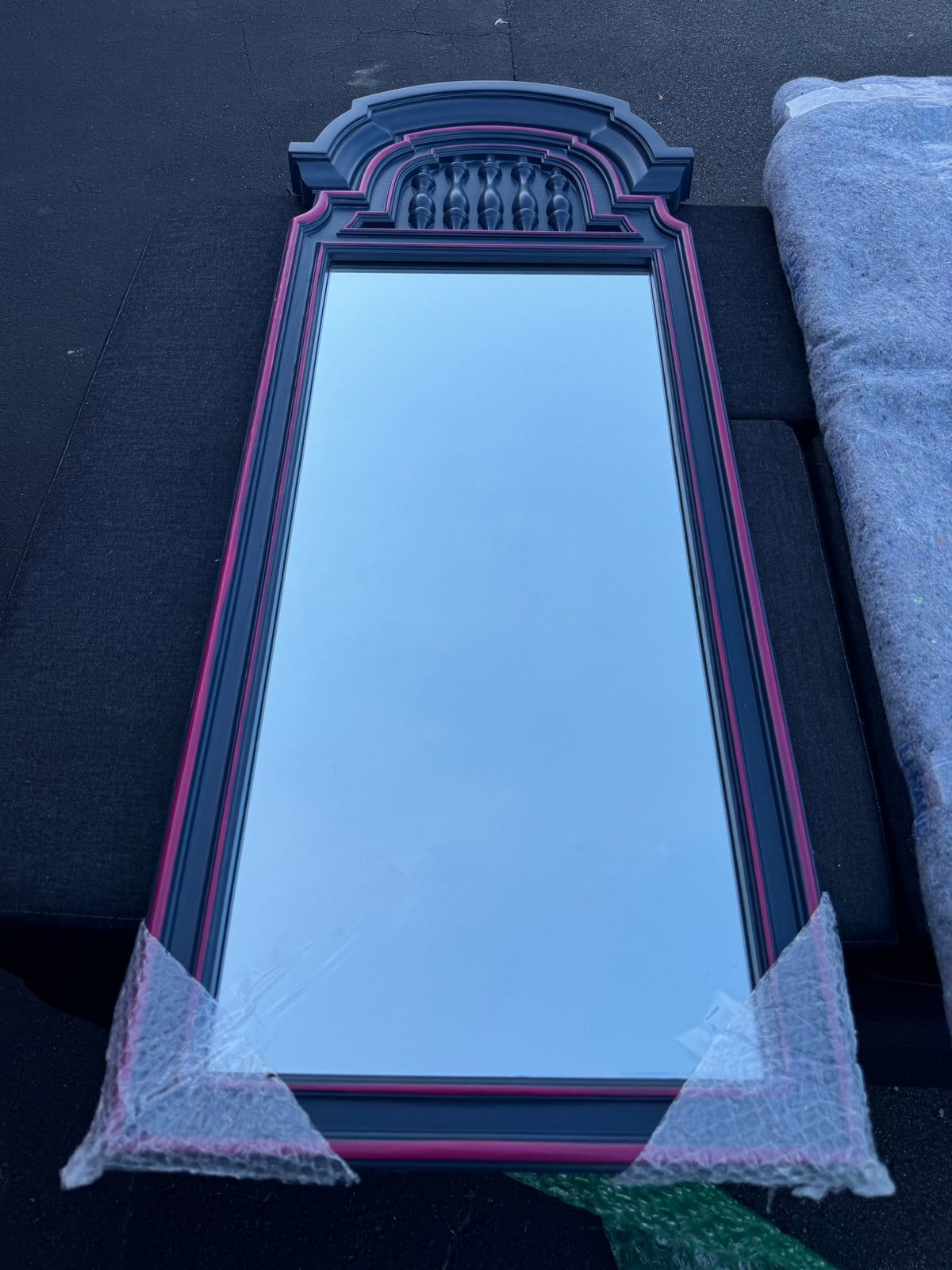 Tall arched mirror with pink and navy frame, ornamental carved crown detail, wrapped in protective plastic