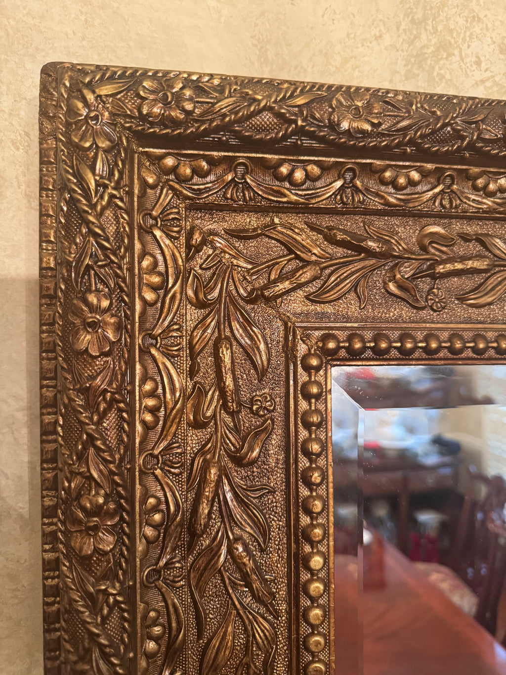 Close-up of the corner of the gilt mirror frame showing embossed floral and beaded relief detail