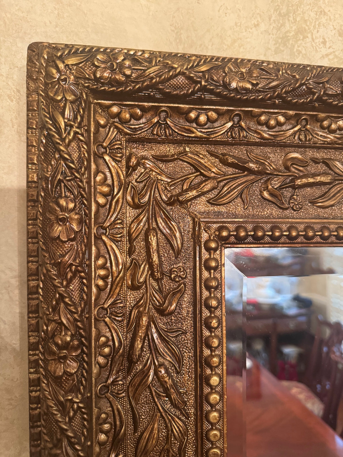 Close-up of the corner of the gilt mirror frame showing embossed floral and beaded relief detail
