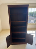 Tall mahogany bookcase with open shelving upper section and closed cabinet base with oval inlaid panels, front view