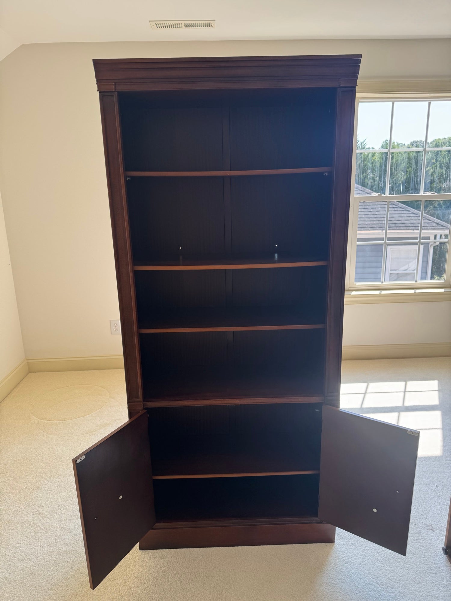 Tall mahogany bookcase with open shelving upper section and closed cabinet base with oval inlaid panels, front view
