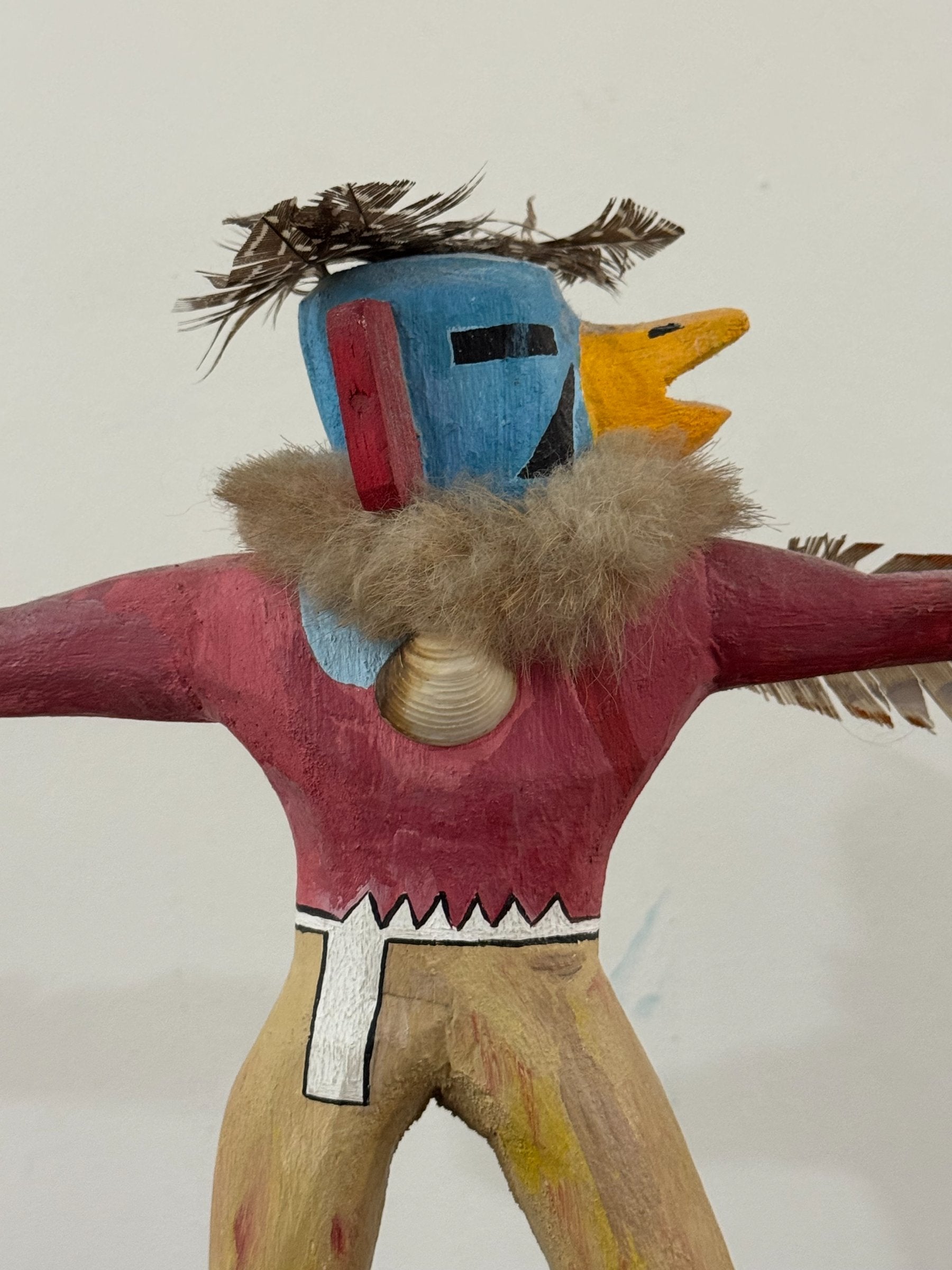 Full figure view from front angle showing complete carved kachina with arms spread, feathered wings, and wooden base