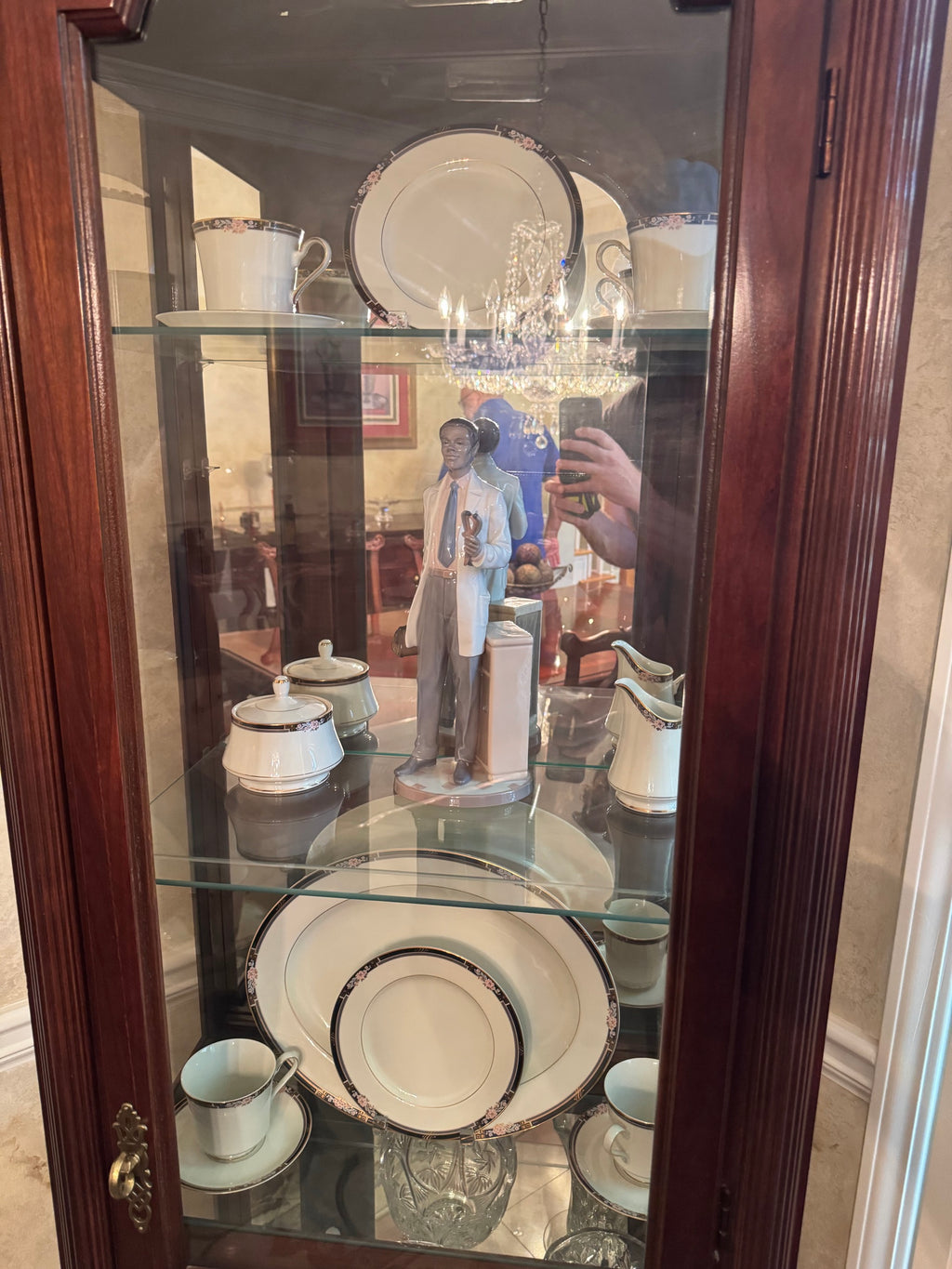 Interior view of the cabinet's upper shelves with china plates, cups, and a porcelain figurine against the mirrored back panel.