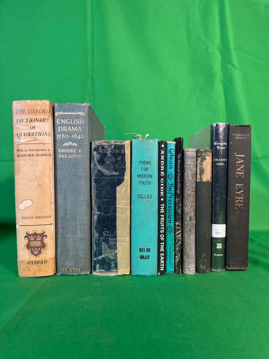 Vintage books stood spine-out on green cloth, including The Oxford Dictionary of Quotations, The Oxford Book of English Verse, Jane Eyre by Charlotte Brontë and The Procession by Kahlil Gibran