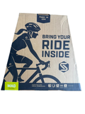 Cardboard shipping box front featuring cyclist illustration, navy and cream design, 'Bring Your Ride Inside' text, made in USA