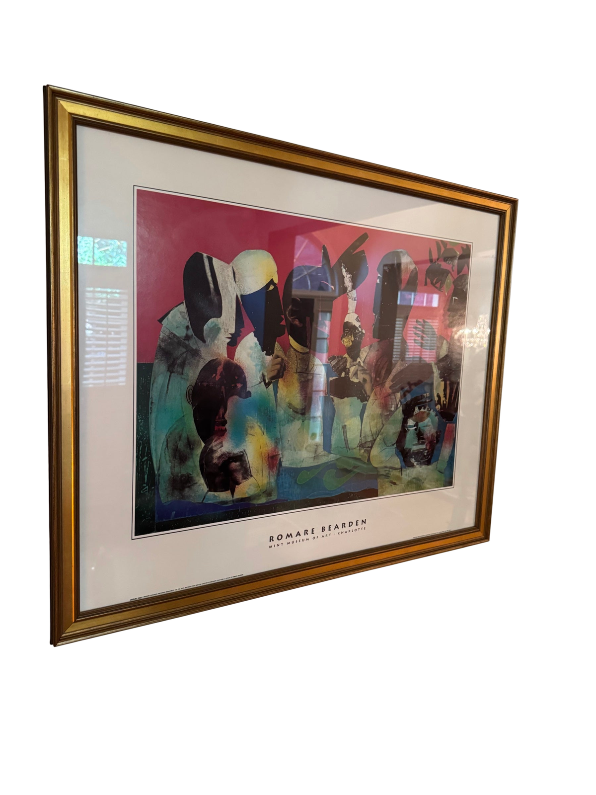 Framed Romare Bearden 'Carolina Shout' exhibition poster from the Mint Museum of Art in a gold frame, viewed at an angle on a wall