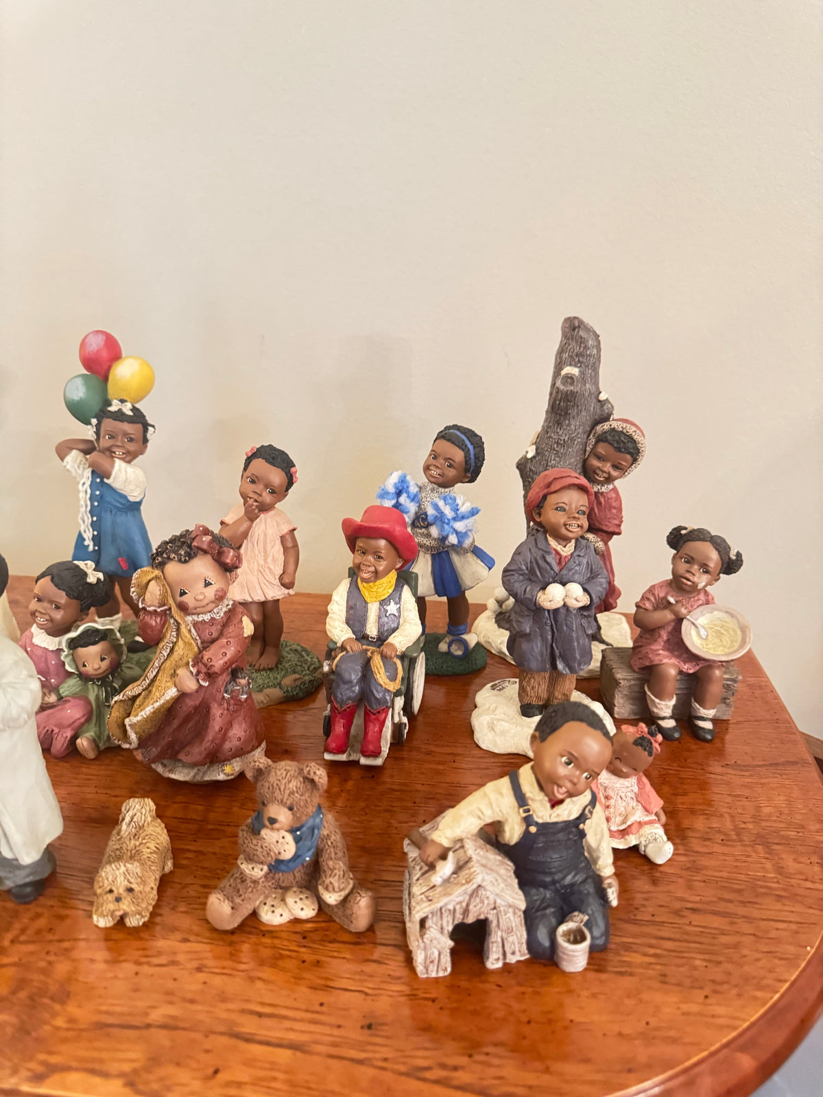 Close view of All God's Children figurines on a wood table showing a cheerleader, a boy in overalls, and a girl holding a doll