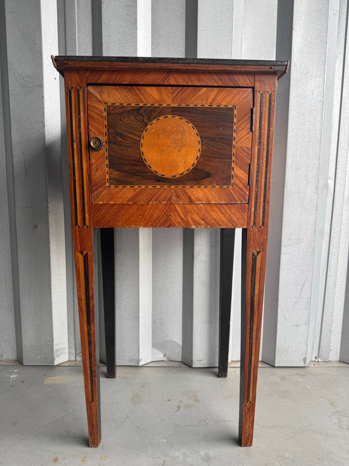 Complete nightstand from front, showing single drawer with portrait medallion, vertical fluting on legs, and tall proportions
