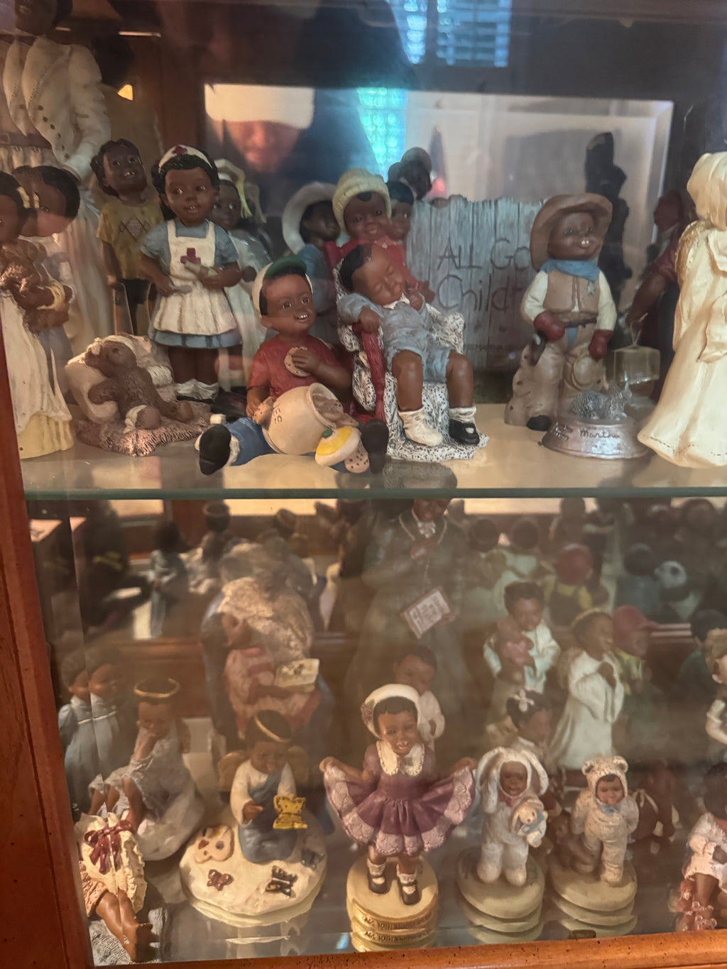 Two shelves of All God's Children figurines depicting children, a nurse, a cowboy, and a wooden fence sign reading All God's Children