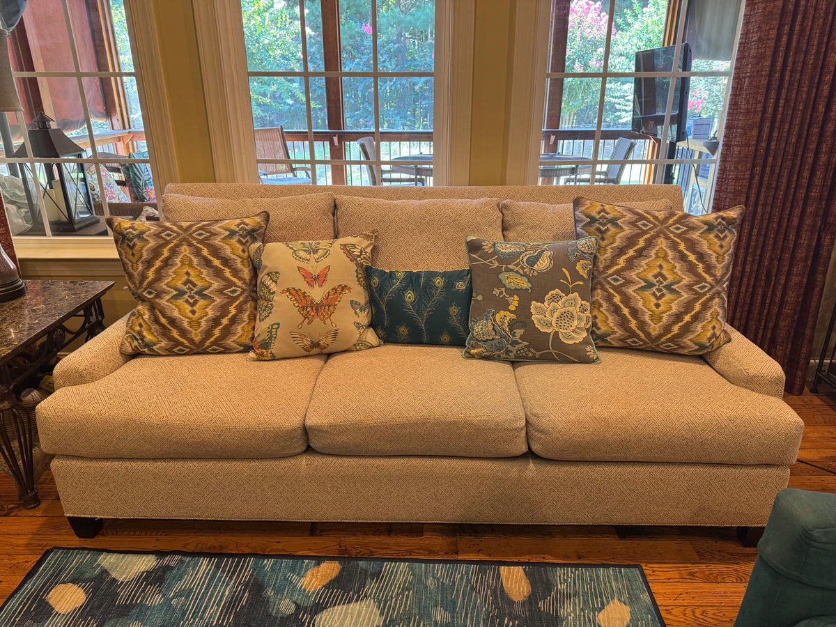 Front view of three-cushion sofa with oatmeal textured upholstery, rolled arms, and decorative patterned pillows in gold and jewel tones