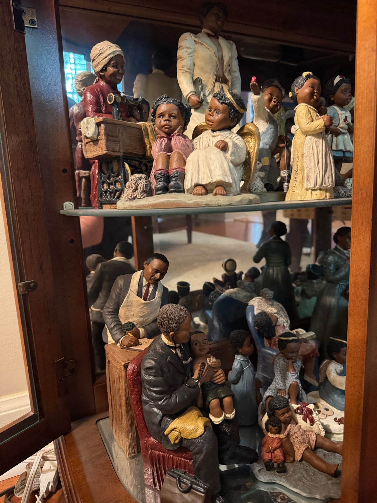 Close view of All God's Children figurines showing an angel, a girl with a sewing machine, and a seated man holding a child