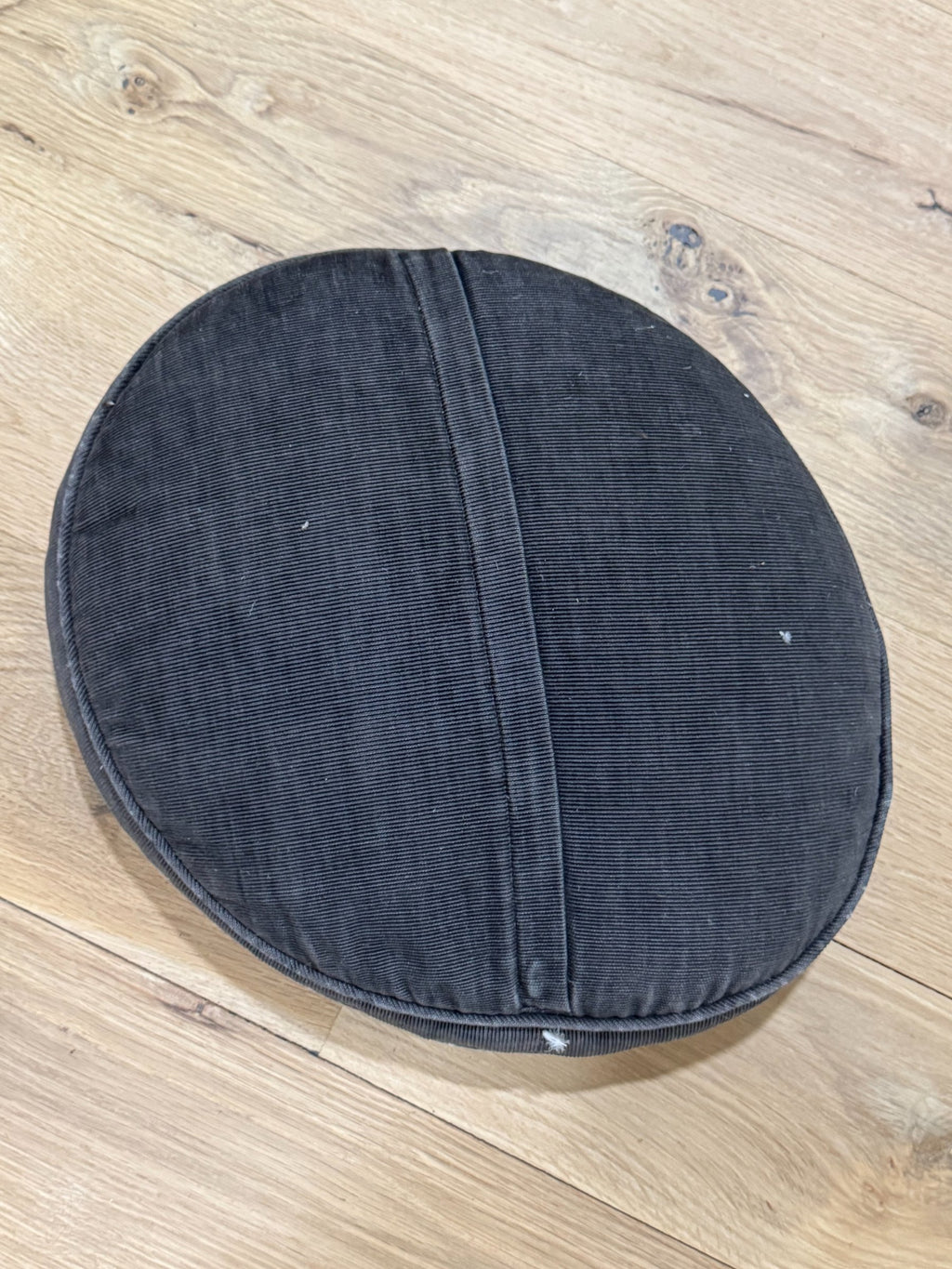 Reverse side of round pillow showing plain dark gray ribbed fabric backing and seaming detail