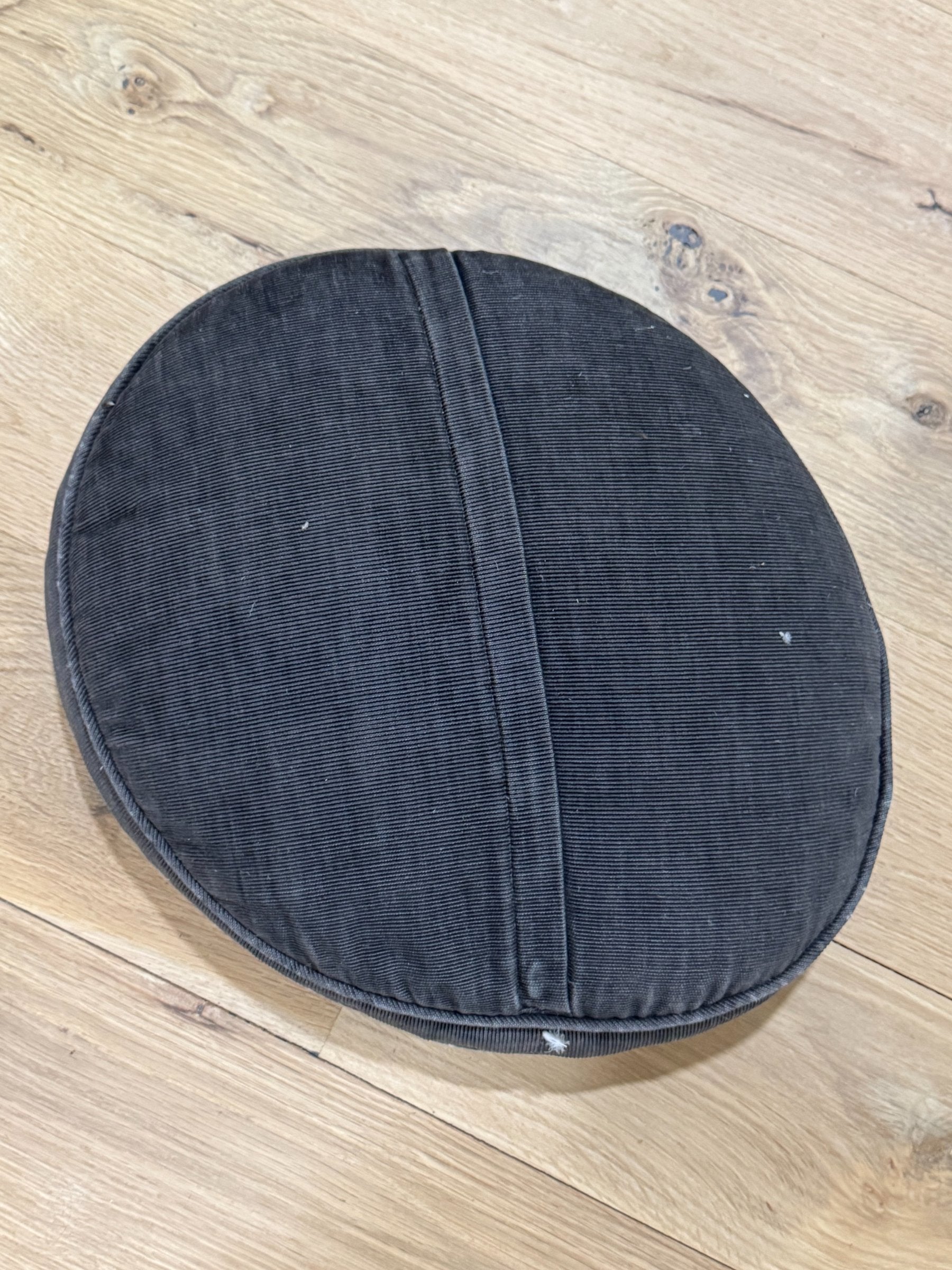 Reverse side of round pillow showing plain dark gray ribbed fabric backing and seaming detail