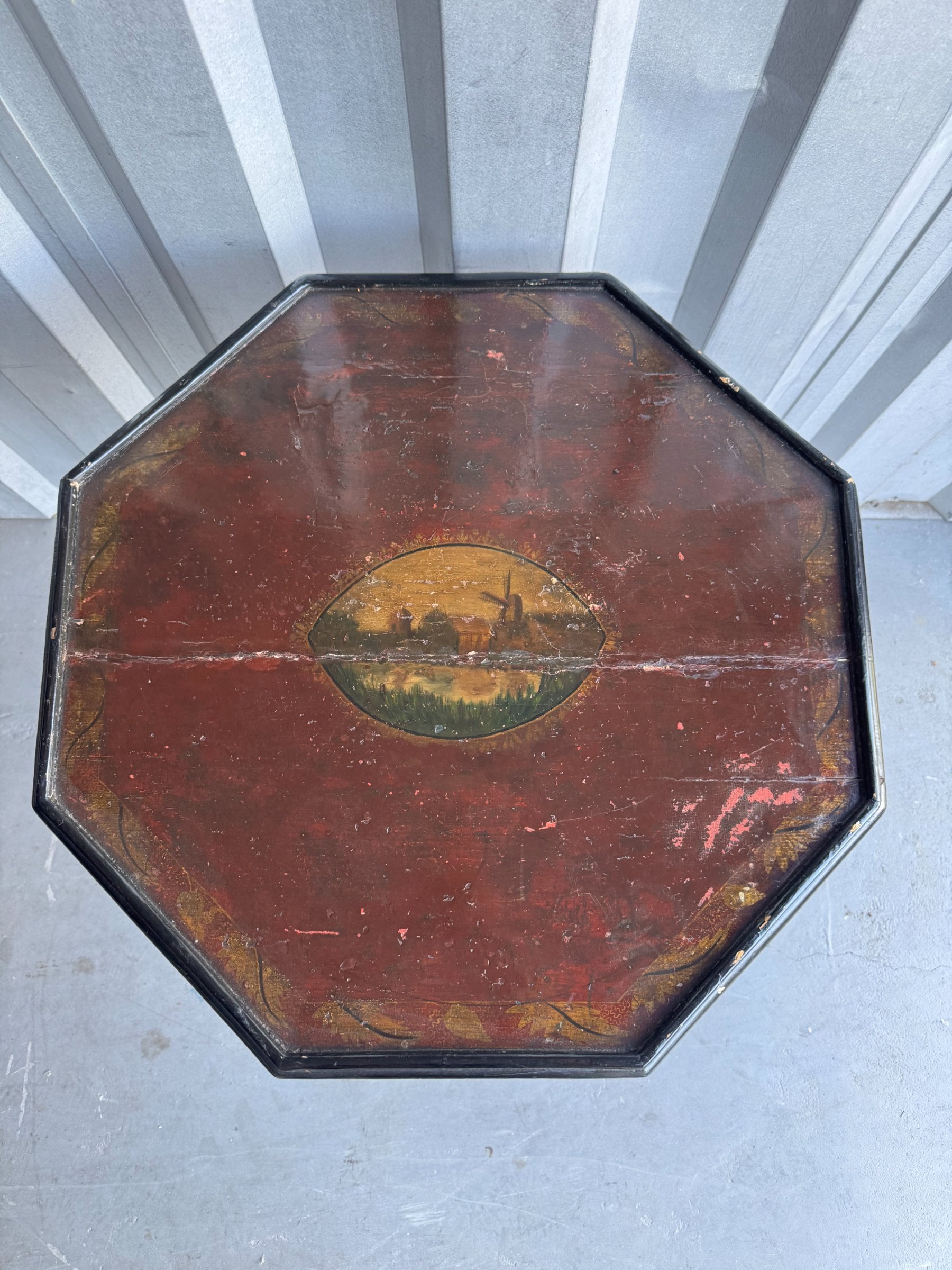 Hand-painted landscape scene on table top featuring golden sunset, green fields, and building silhouette
