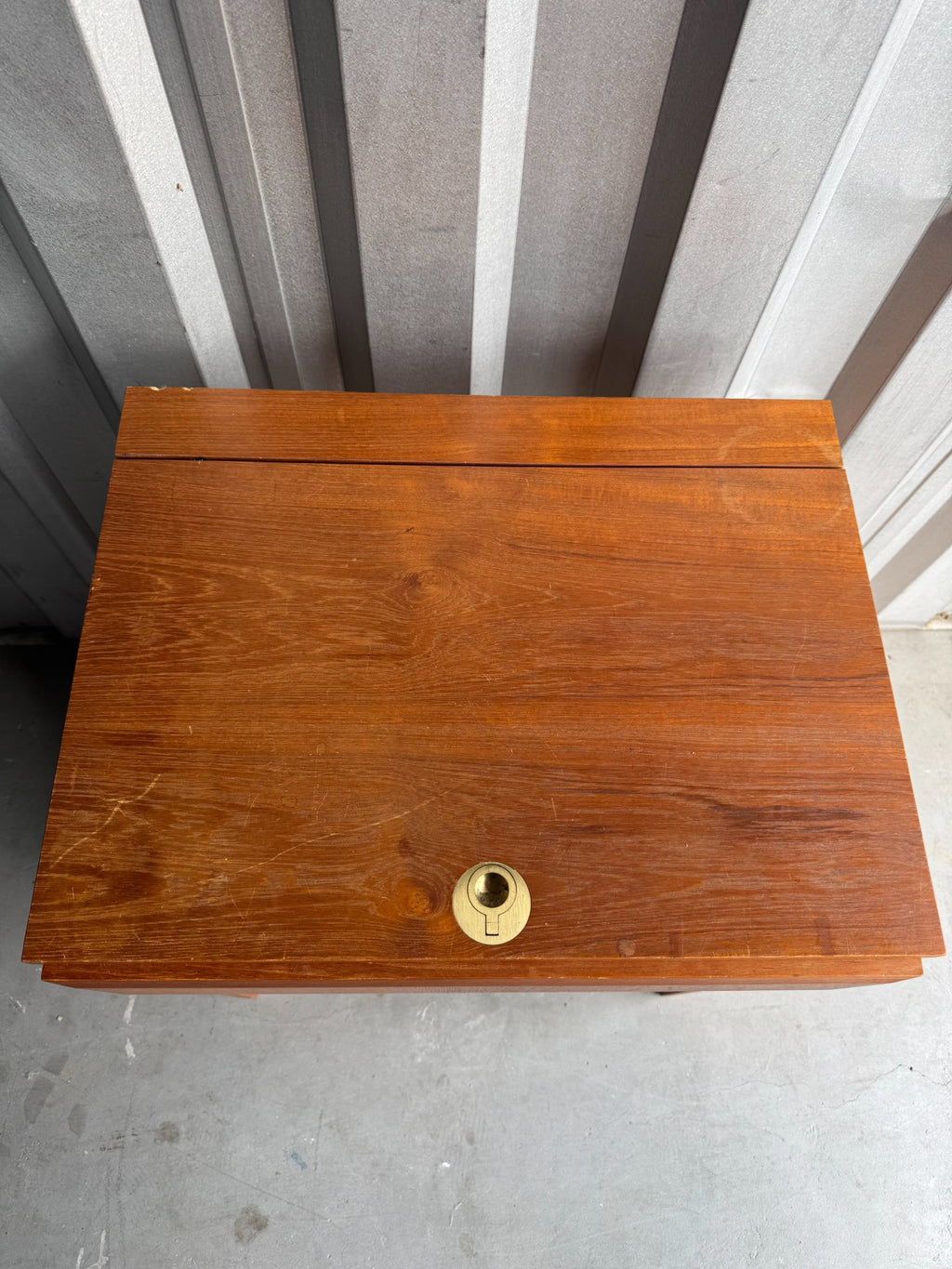 Top surface of closed desk showing teak wood grain, brass keyhole hardware, and hinged panel detail