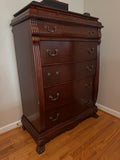 Mahogany finish tall chest with five drawers, brass hardware, reeded columns, and carved claw feet, shown at an angle in a bedroom