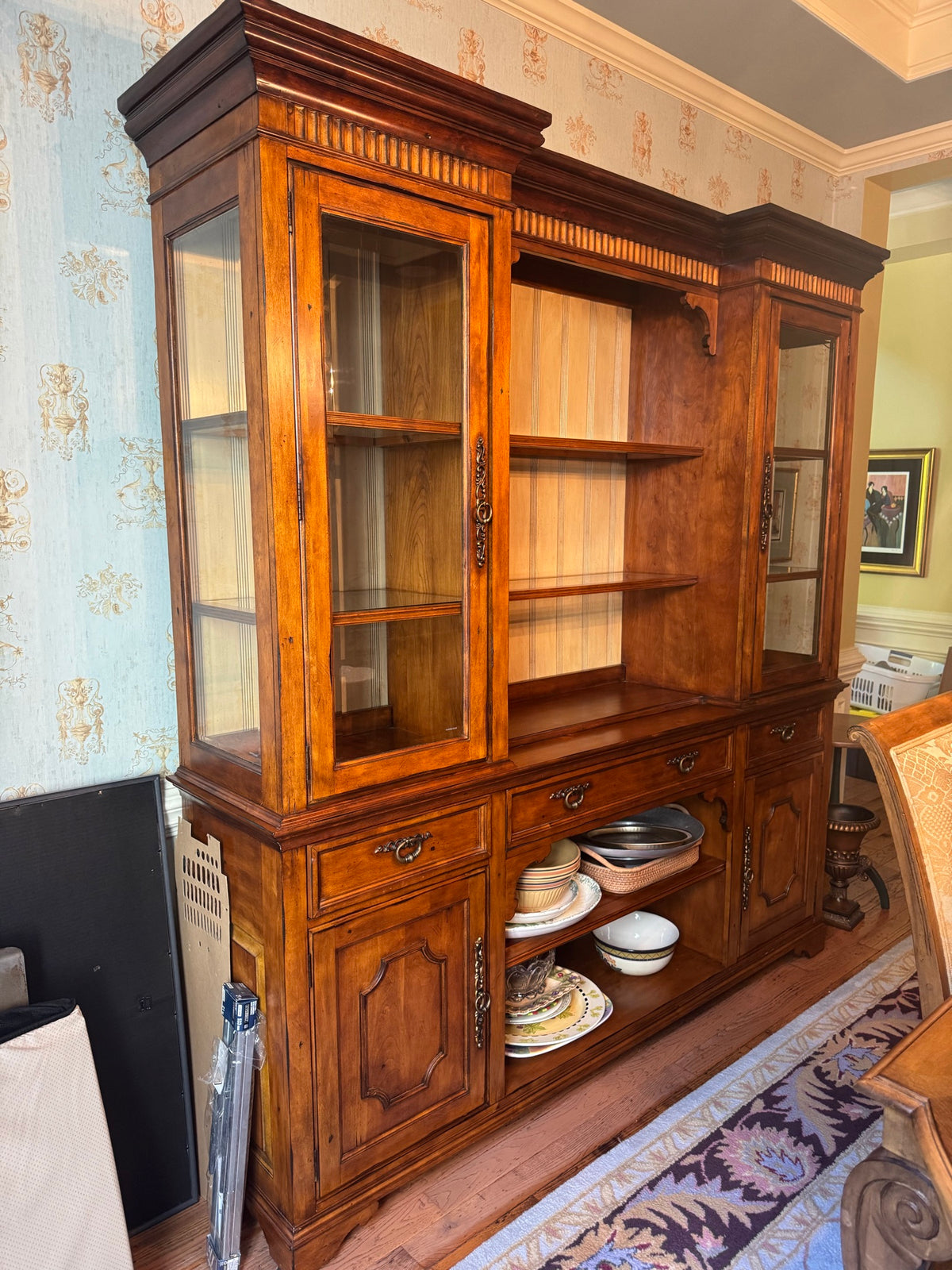 Angled front view showing glass-fronted left cabinet, open center shelving with wood backing, right glass cabinet, lower closed storage with dishes inside