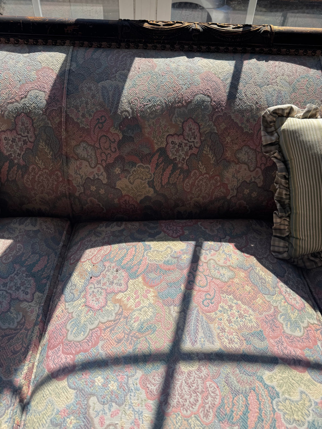 Close-up of sofa cushions and fabric showing floral damask pattern in burgundy, cream, and blue tones with shadow play from window