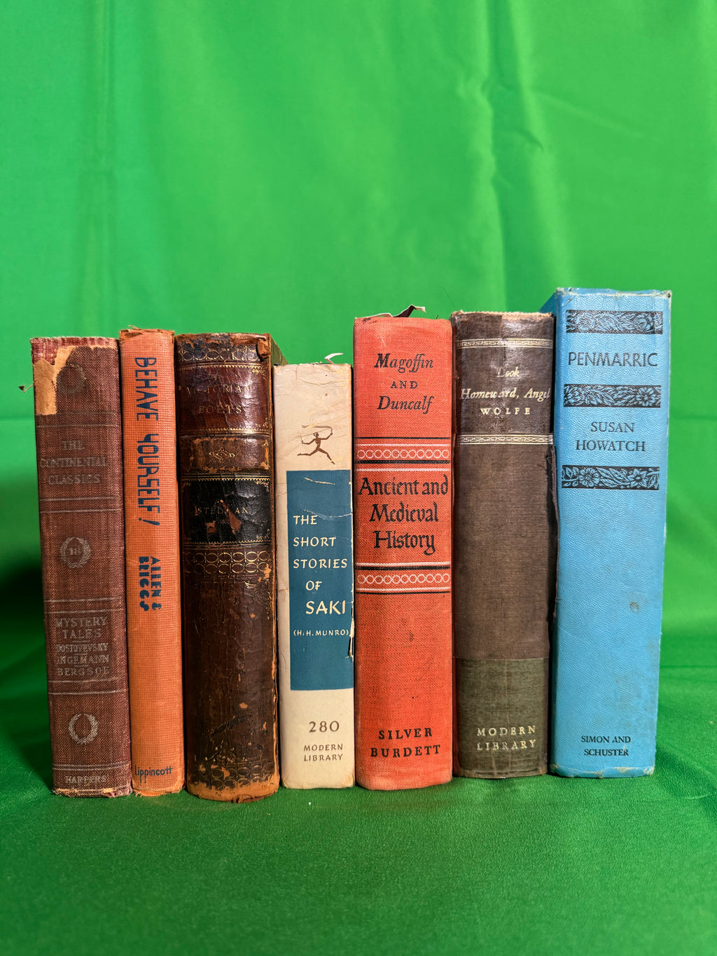 Vintage hardcovers stood spine-out on green cloth, including a Modern Library Look Homeward, Angel by Thomas Wolfe, The Short Stories of Saki, Victorian Poets in worn leather, and Penmarric by Susan Howatch