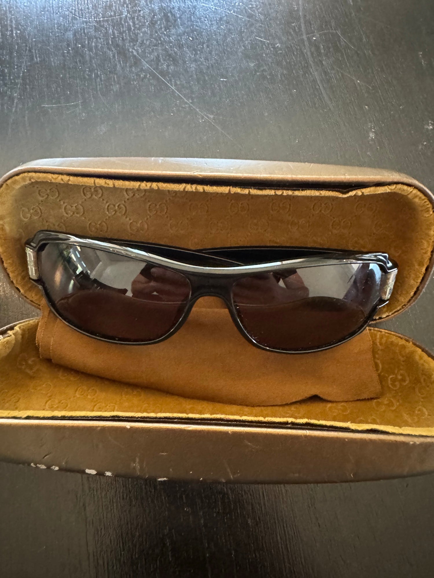 Gucci sunglasses with tortoiseshell and clear frames, dark lenses, resting on tan velvet case interior