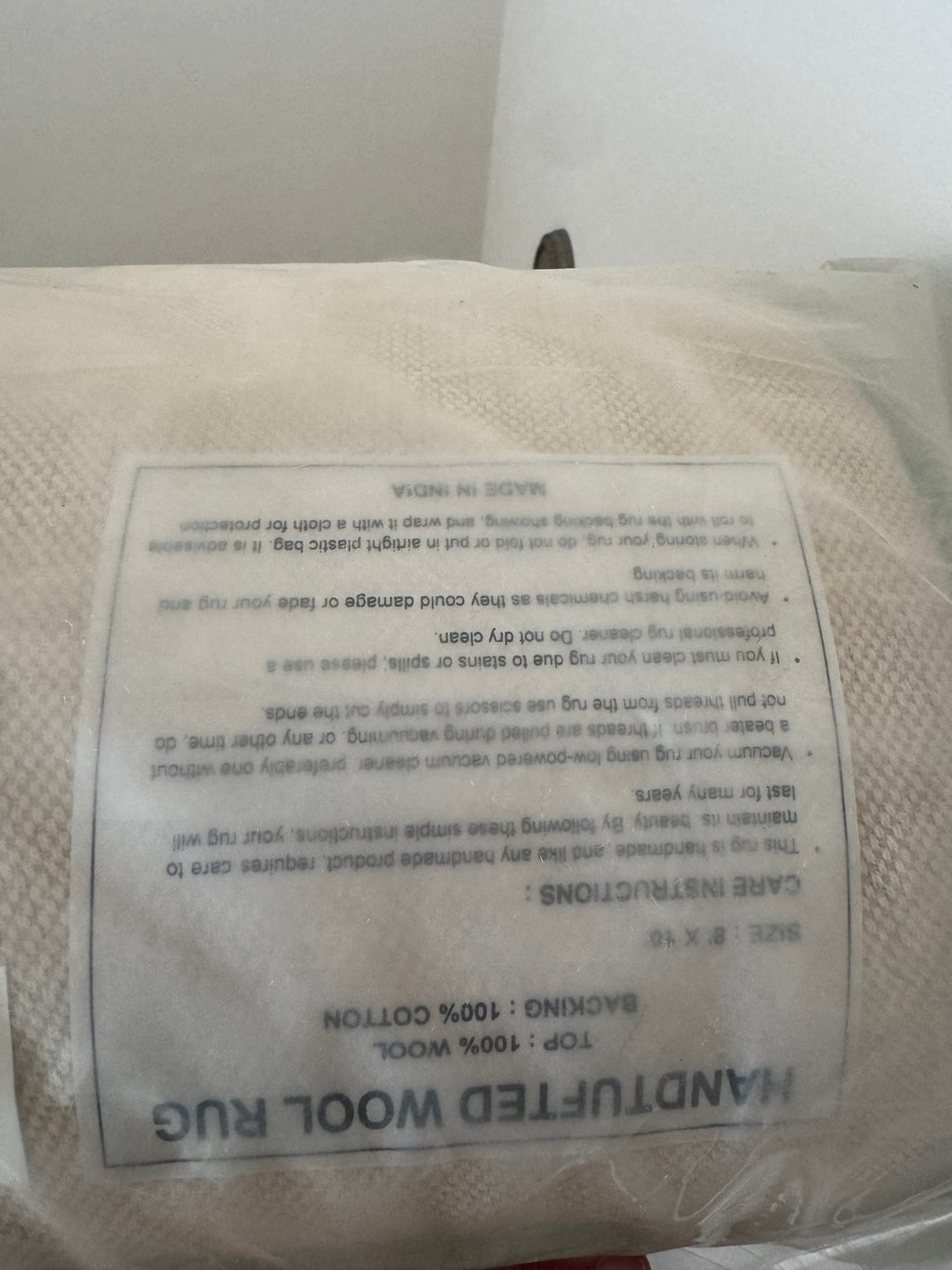 Care instructions label on cream wool rug, text includes fiber content 100% wool and cleaning guidelines