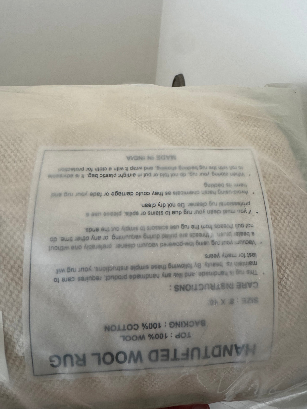 Care instructions label on cream wool rug, text includes fiber content 100% wool and cleaning guidelines